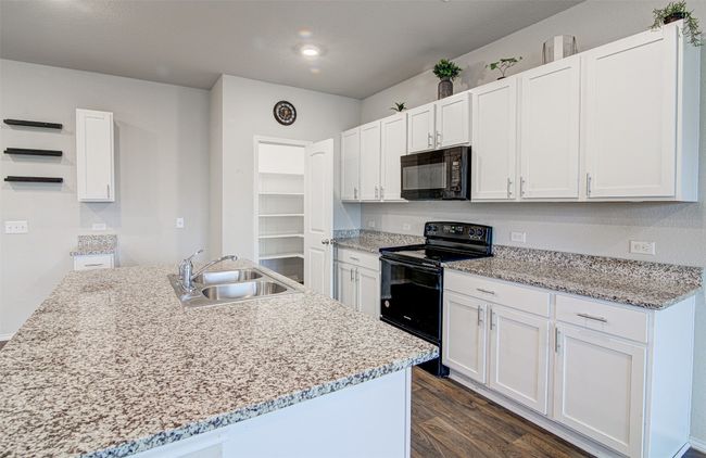 Kitchen with dark wood-style flooring, white cabinetry, black appliances, a center island with sink, and a sink | Image 14