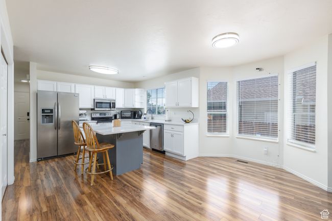 Kitchen featuring appliances with stainless steel finishes, white cabinetry, light countertops, a kitchen island, and a kitchen bar | Image 7