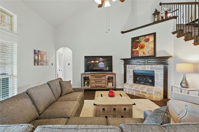 Living room with high vaulted ceiling, wood finished floors, arched walkways, ceiling fan, and a fireplace with raised hearth | Image 16