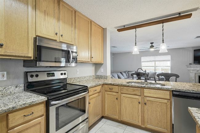 Kitchen featuring stainless steel appliances, ceiling fan, open floor plan, light tile patterned floors, and light stone countertops | Image 13