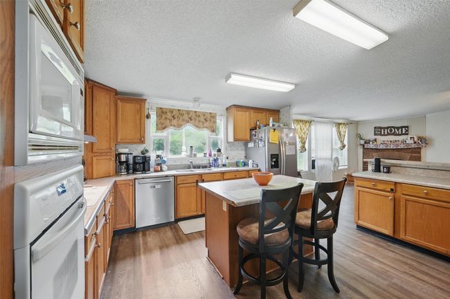 Kitchen with stainless steel appliances, a textured ceiling, light countertops, wood finished floors, and a center island | Image 7