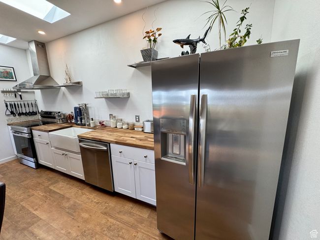 Kitchen featuring stainless steel appliances, butcher block countertops, open shelves, a skylight, and exhaust hood | Image 6