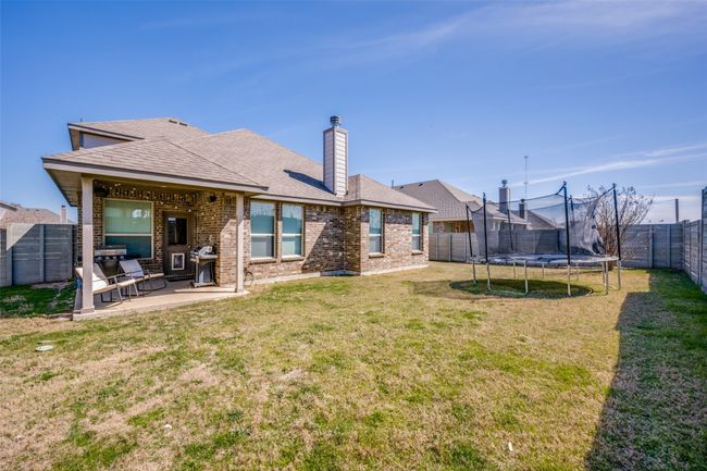 Rear view of property featuring a lawn, a trampoline, a fenced backyard, brick siding, and a patio area | Image 34