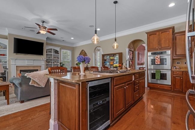 Kitchen with beverage cooler, stainless steel appliances, arched walkways, dark wood-style flooring, and light stone counters | Image 17