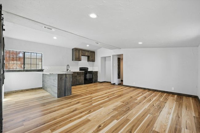 Kitchen with visible vents, light wood finished floors, black electric range oven, a peninsula, and light countertops | Image 14