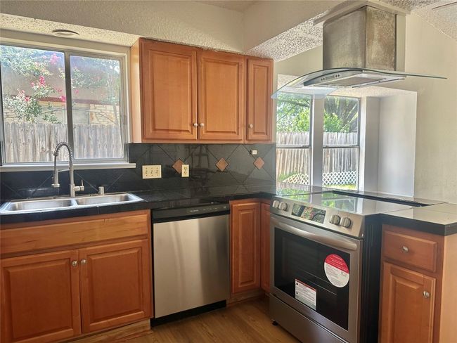 Kitchen featuring appliances with stainless steel finishes, island range hood, a peninsula, wood finished floors, and brown cabinetry | Image 4