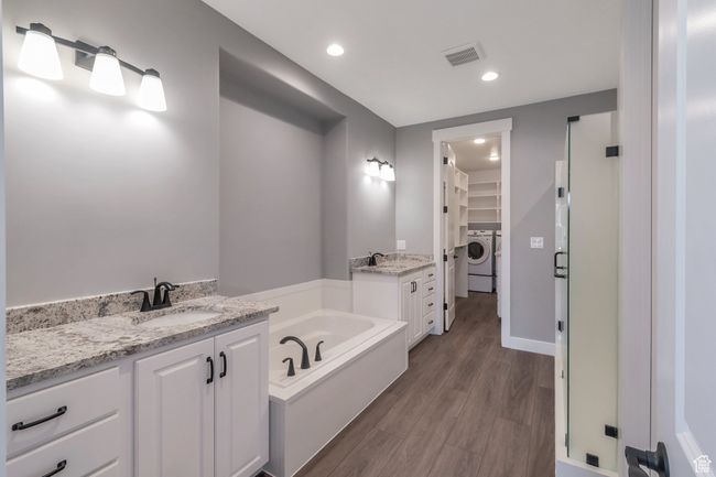 Bathroom with washer / dryer, a walk in closet, vanity, a bath, and wood finished floors | Image 19