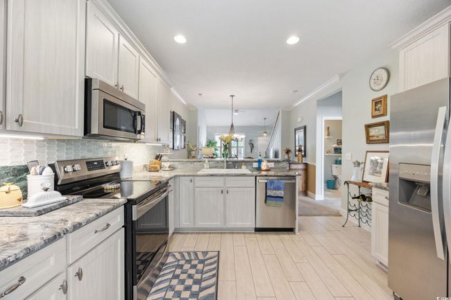 Kitchen featuring appliances with stainless steel finishes, a peninsula, crown molding, white cabinetry, and light wood finished floors | Image 12