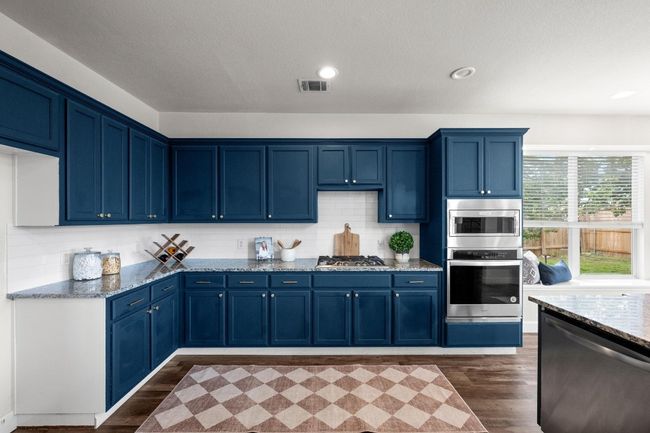 Kitchen featuring stainless steel appliances, blue cabinetry, light stone counters, dark wood finished floors, and recessed lighting | Image 5