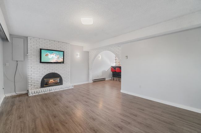 Unfurnished living room with a textured ceiling, a fireplace, wood finished floors, baseboards, and baseboard heating | Image 28