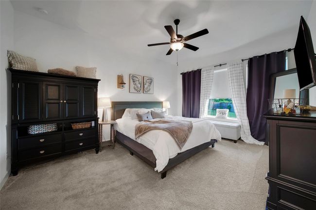 This cozy bedroom features a plush carpet, a large bed with neutral bedding, and elegant dark wood furniture. Natural light streams in through the window with stylish curtains, creating a warm and inviting atmosphere. | Image 30