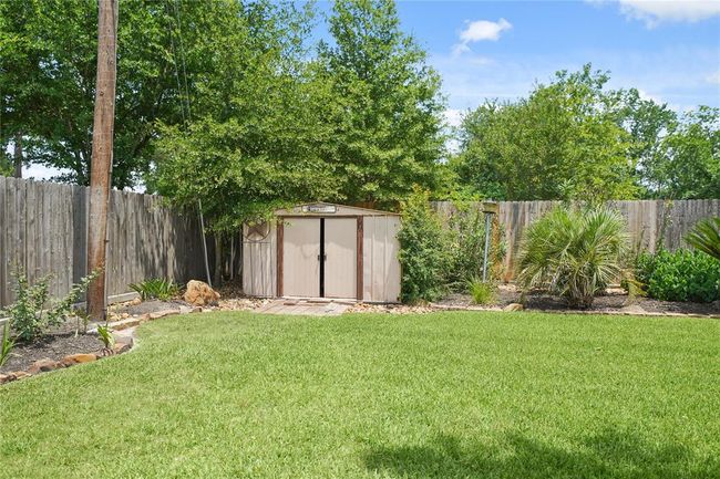 Spacious backyard with well-maintained lawn, lush greenery, and a wooden storage shed, perfect for outdoor activities and storage needs. | Image 30