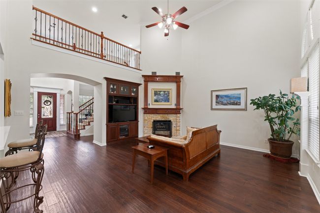 Living area featuring a stone fireplace, a ceiling fan, a towering ceiling, arched walkways, and stairs | Image 4