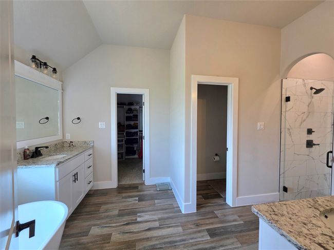 Full bath with a stall shower, vanity, wood finished floors, a walk in closet, and vaulted ceiling | Image 24