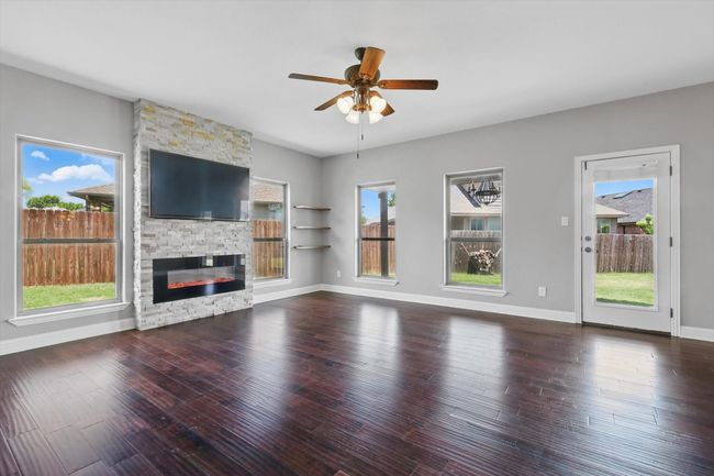 Unfurnished living room with a ceiling fan, hardwood / wood-style flooring, a fireplace, and baseboards | Image 12