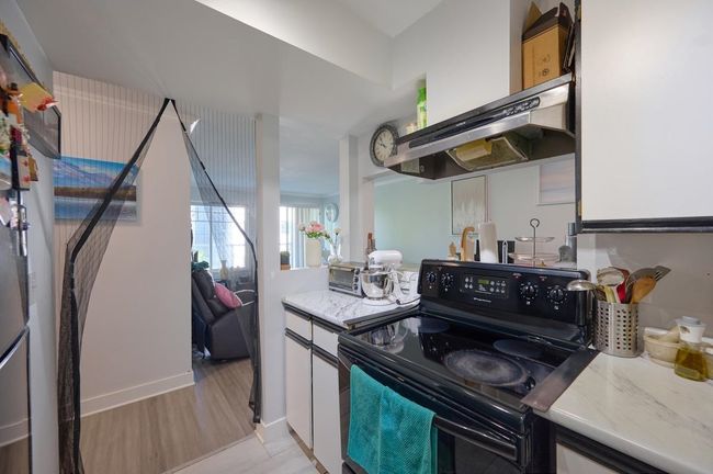 Kitchen with exhaust hood, black / electric stove, light stone counters, light wood finished floors, and white cabinets | Image 10