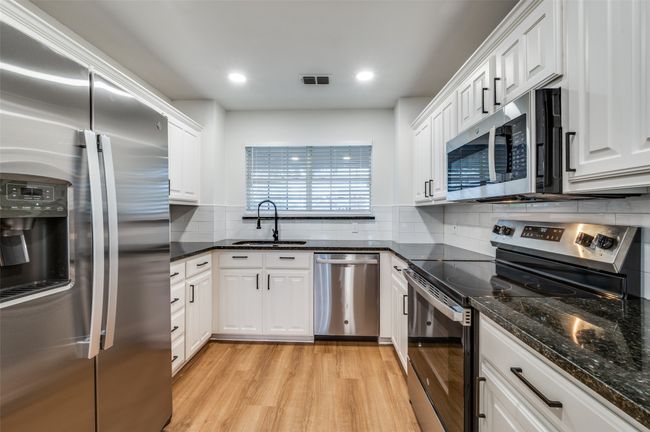 Kitchen featuring light wood-style flooring, white cabinetry, appliances with stainless steel finishes, a sink, and backsplash | Image 11