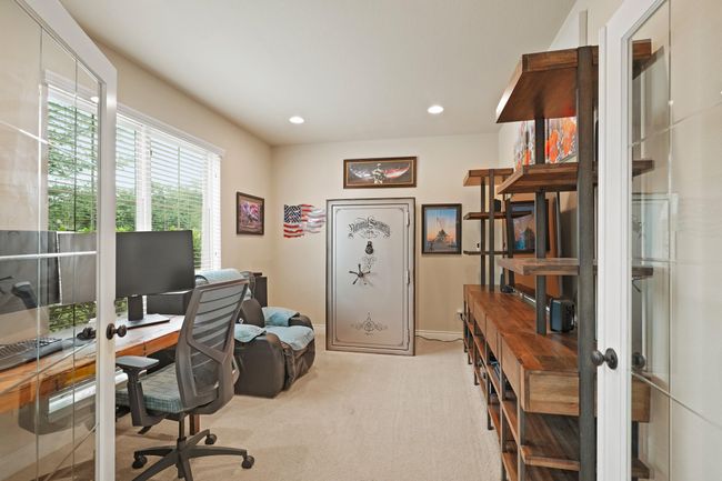 This photo showcases a well-lit home office with large windows. The room has neutral walls and carpet, providing a functional and organized workspace. (The safe doesn't convey). | Image 7