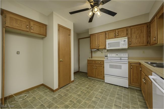 Kitchen with white appliances, brown cabinets, light countertops, ceiling fan, and light floors | Image 10