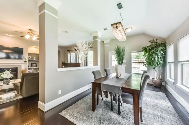 Bright and modern dining area with large windows, a stylish chandelier, and an open layout leading to a cozy living room with a fireplace. Ideal for entertaining. | Image 16