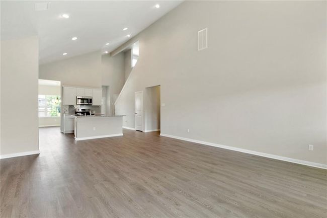 Unfurnished living room with wood finished floors, recessed lighting, baseboards, and high vaulted ceiling | Image 11