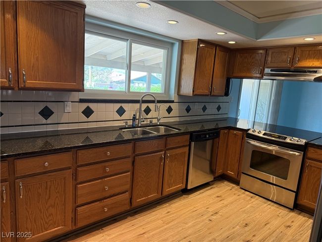 Kitchen with stainless steel appliances, exhaust hood, a sink, light wood-style floors, and dark stone counters | Image 13