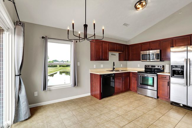 kitchen with appliances, a chandelier, light countertops, reddish brown cabinets, and vaulted ceiling | Image 13