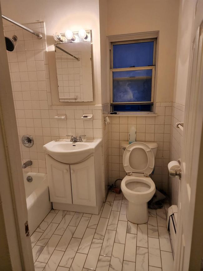 Full bathroom featuring vanity, marble look tiles, bathtub / shower combination, tile walls, and a baseboard heating unit | Image 6