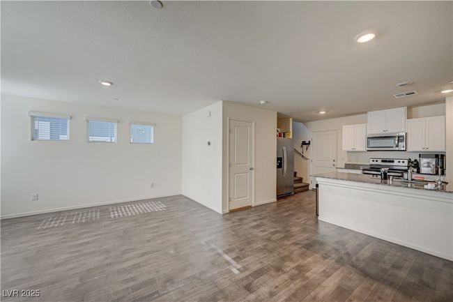 Kitchen with appliances with stainless steel finishes, wood finished floors, white cabinets, open floor plan, and light stone countertops | Image 5