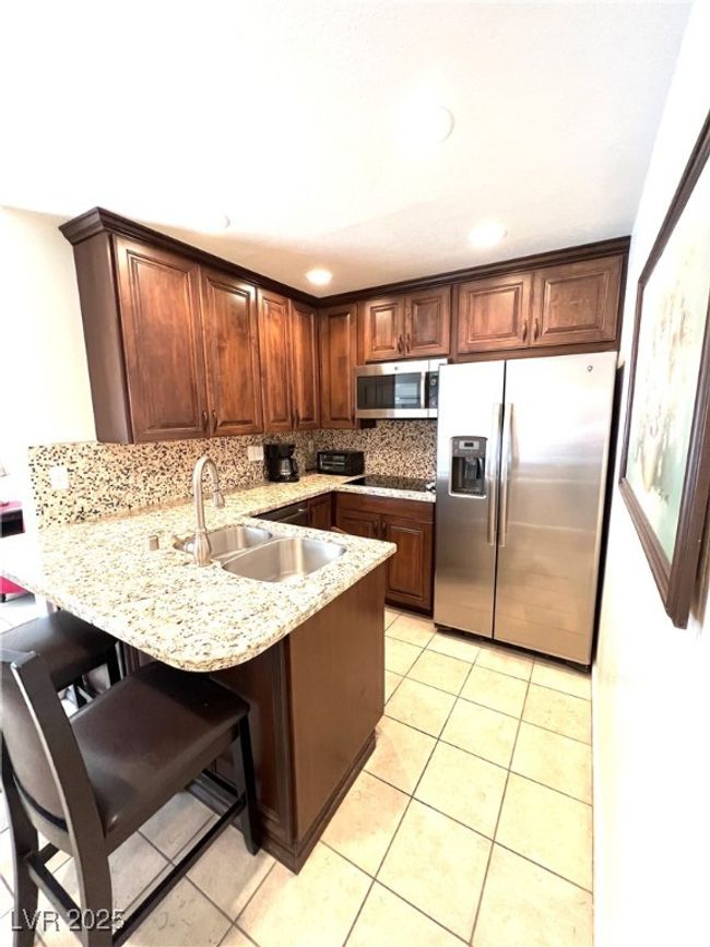 Kitchen with light tile patterned flooring, a sink, appliances with stainless steel finishes, and a peninsula | Image 23