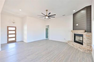 Unfurnished living room with wood-type flooring, ceiling fan with notable chandelier, and a brick fireplace | Image 3