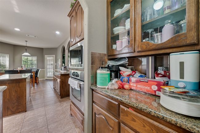 Kitchen with appliances with stainless steel finishes, light stone counters, glass insert cabinets, light tile patterned flooring, and pendant lighting | Image 12