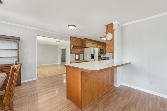 Kitchen featuring appliances with stainless steel finishes, light wood finished floors, a peninsula, ornamental molding, and brown cabinets | Image 12