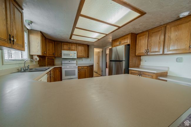 Kitchen featuring brown cabinets, light countertops, a sink, white appliances, and a textured ceiling | Image 8