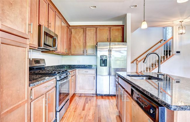 Kitchen featuring appliances with stainless steel finishes, a sink, hardwood flooring, granite counters, and a center island with sink | Image 11