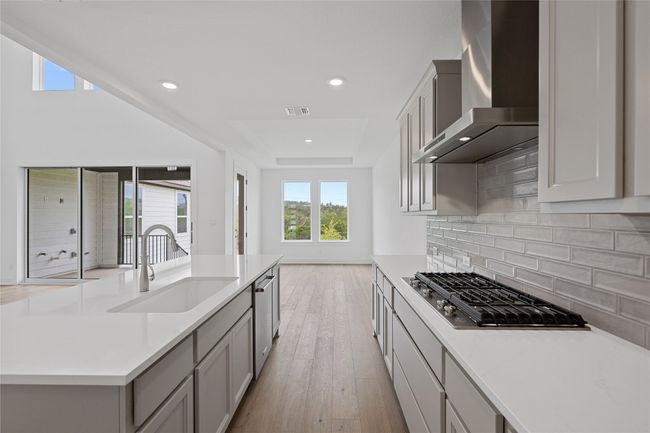 Kitchen with wall chimney exhaust hood, a sink, appliances with stainless steel finishes, decorative backsplash, and light countertops | Image 9