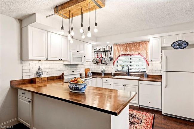 Kitchen with wooden counters, a textured ceiling, white appliances, a peninsula, and backsplash | Image 11