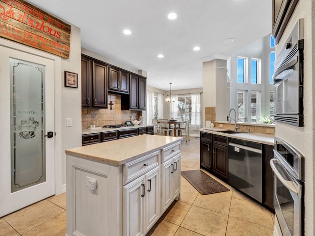 Kitchen with tile floors, backsplash, appliances with stainless steel finishes, a sink, and cabinets | Image 18
