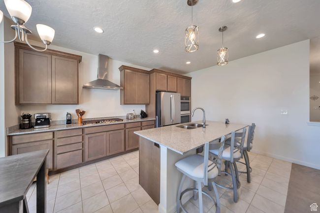 Kitchen with wall chimney exhaust hood, stainless steel appliances, a sink, light stone countertops, and light tile patterned floors | Image 4