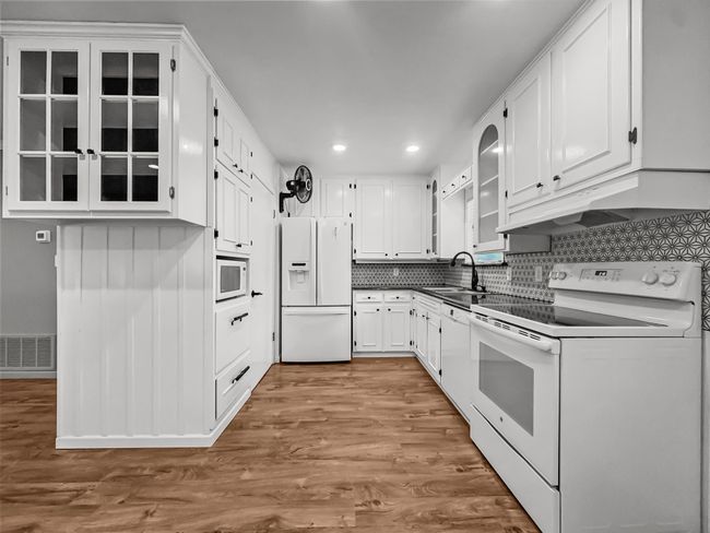 Kitchen featuring white appliances, white cabinetry, recessed lighting, wood finished floors, and dark countertops | Image 4