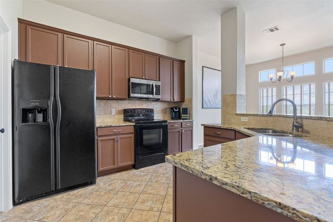 Kitchen featuring tasteful backsplash, a chandelier, a sink, light stone countertops, and black appliances | Image 26