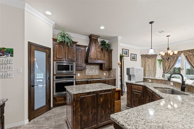 Kitchen with stainless steel appliances, a sink, a center island, custom range hood, and a chandelier | Image 5