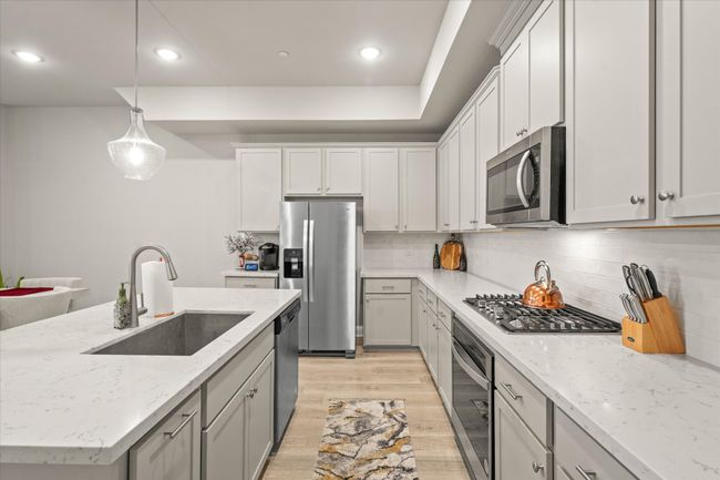 Kitchen featuring appliances with stainless steel finishes, light wood-type flooring, backsplash, pendant lighting, and light stone countertops | Image 8