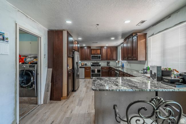 Kitchen with appliances with stainless steel finishes, washer / dryer, light wood finished floors, a peninsula, and a textured ceiling | Image 22