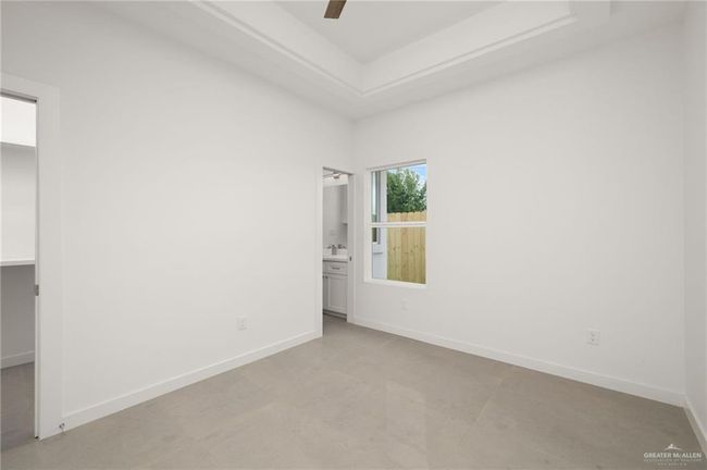 Unfurnished bedroom featuring a spacious closet, ensuite bathroom, a tray ceiling, and a ceiling fan | Image 11