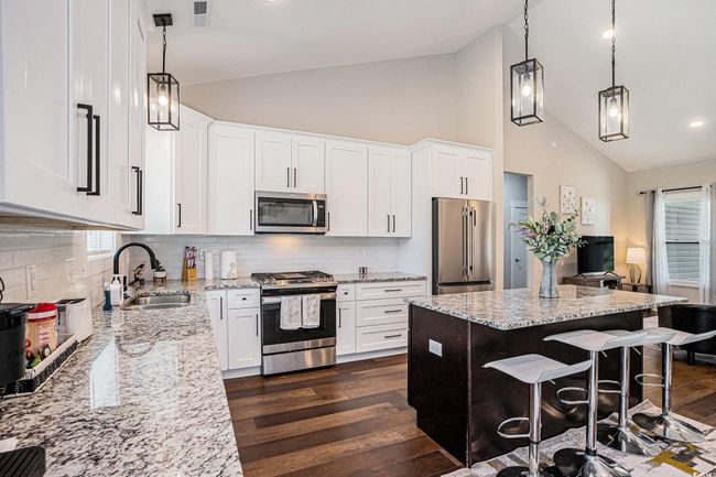Kitchen featuring appliances with stainless steel finishes, dark wood-type flooring, light stone countertops, a breakfast bar area, and high vaulted ceiling | Image 8