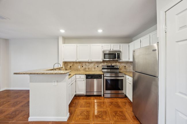 Kitchen featuring stainless steel appliances, a peninsula, white cabinetry, tumbled marble backsplash, and light granite countertops | Image 8
