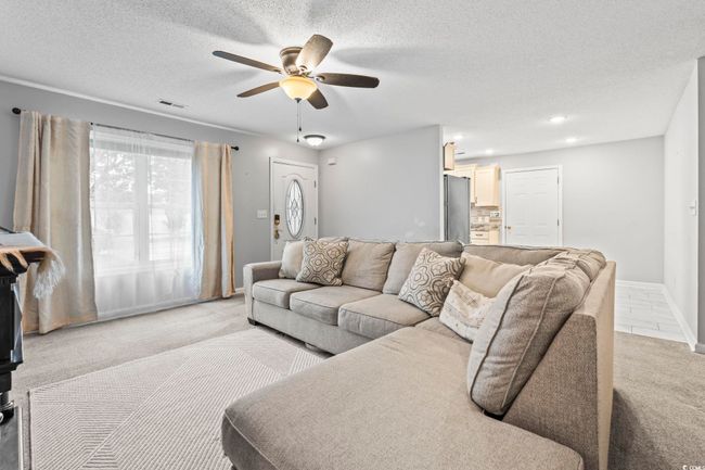 Living room featuring light colored carpet, ceiling fan, and a textured ceiling | Image 6
