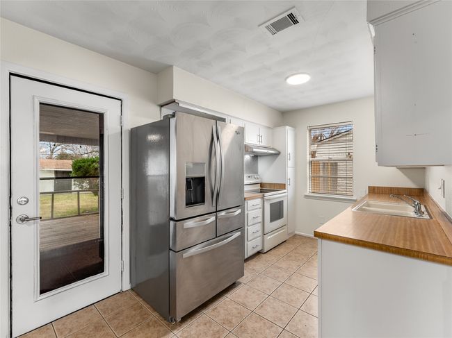 Kitchen with sink, light tile patterned floors, stainless steel fridge, white range with electric cooktop, and white cabinetry | Image 13