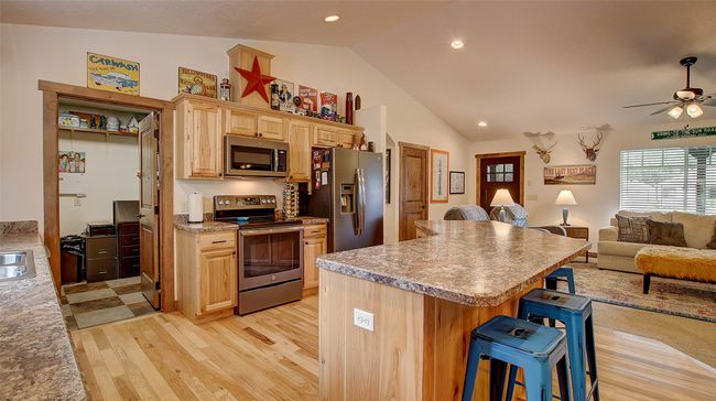 Kitchen with stainless steel appliances, open floor plan, a kitchen breakfast bar, light wood-type flooring, and a kitchen island | Image 11